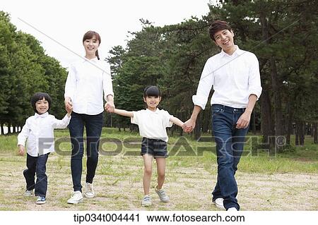 Stock Image - Family walking hand in hand on grass with trees behind. Fotosearch