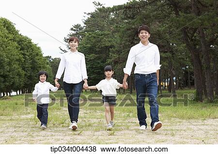 Stock Photo - Family walking hand in hand on grass with trees behind. Fotosearch