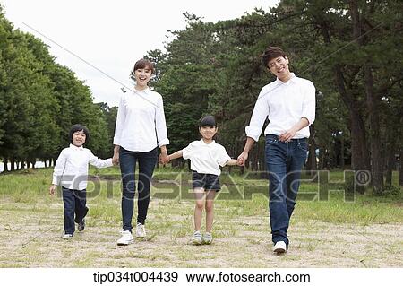 Family walking hand in hand on grass with trees behind View Large Photo Image Stock Photo - Family walking hand in hand on grass with trees behind. Fotosearch