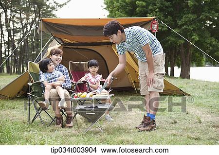 father grilling while other family members sat on camping chairs View Large Photo Image Picture - father grilling while other family members sat on camping chairs . Fotosearch