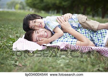 Picture - father lying on a picnic blanket with a son lying on him. Fotosearch