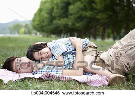 Stock Photograph - father lying on a picnic blanket with a son lying on him. Fotosearch