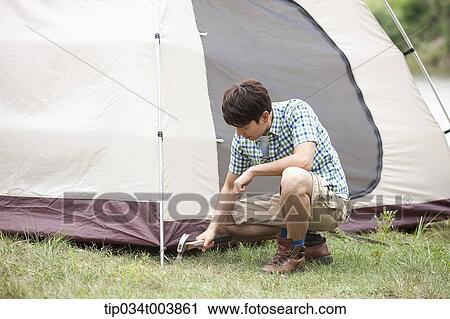 Stock Image - father using hammer to build a tent. Fotosearch