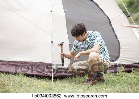 Stock Image - father using hammer to build a tent. Fotosearch
