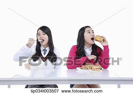 Stock Photo - female student having a rice while the other identical female student is having a burger. Fotosearch