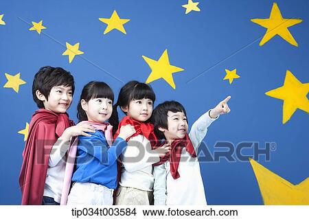 Picture - four kids wearing superman capes standing in a line in front of a blue wall full of stars. Fotosearch