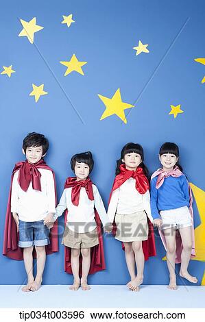 Stock Photograph - four kids wearing superman capes standing in a line with their backs on a wall. Fotosearch