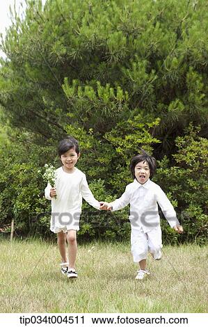Stock Image - kids running on grass hand in hand . Fotosearch