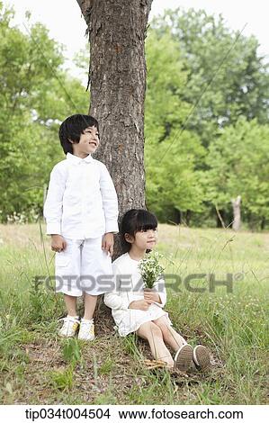 Picture - kids standing and sitting under a tree. Fotosearch