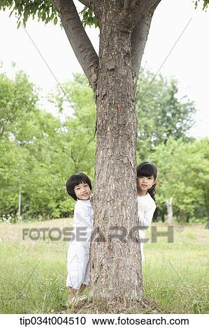 Stock Image - kids standing behind a tree. Fotosearch