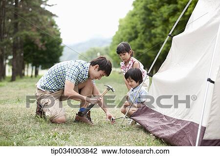 Stock Image - kids watching a father building a tent. Fotosearch