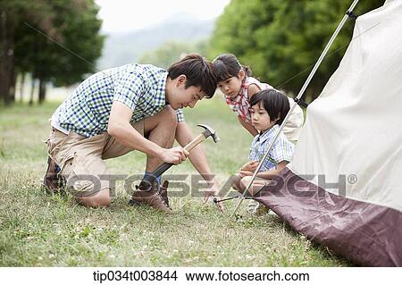 Picture - kids watching a father hammering to build a tent. Fotosearch