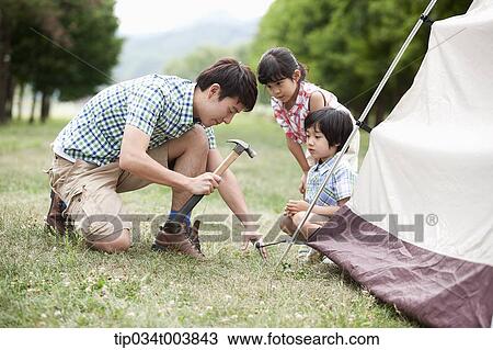 Stock Image - kids watching a father hammering to build a tent. Fotosearch