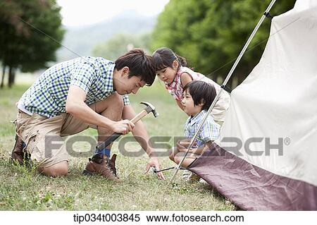 Stock Photography - kids watching a father hammering to build a tent. Fotosearch