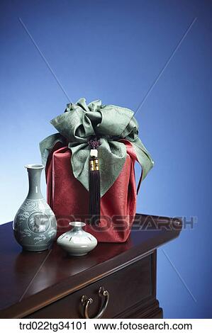 Stock Image - Korean ceramics and a package in a red Korean traditional wrap on a table. Fotosearch