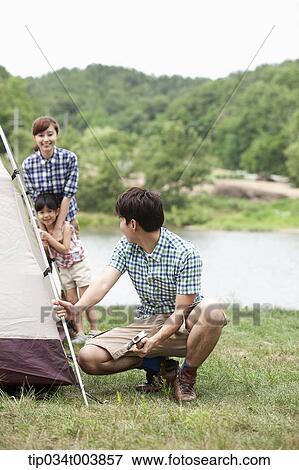 Stock Photo - mother and daughter talking to father building a tent. Fotosearch