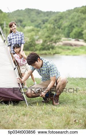 Stock Photograph - mother and daughter watching father building a tent. Fotosearch