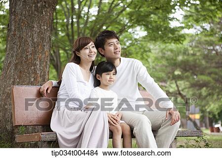 Picture - parents with a female kid sitting on a bench . Fotosearch