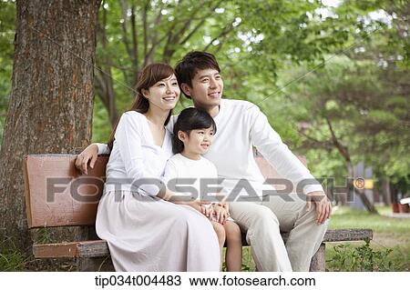 Stock Image - parents with a female kid sitting on a bench . Fotosearch