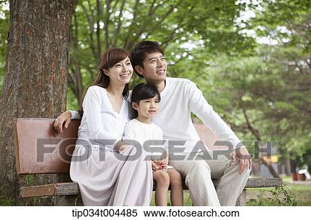 Stock Photography - parents with a female kid sitting on a bench . Fotosearch