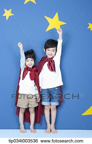 Stock Photograph - two boys wearing red capes raising up their arms like a superman. Fotosearch