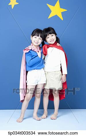 Picture - two girls with superman capes smiling in blue background with stars. Fotosearch