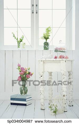 Stock Photo - vase with flowers on a pile of books, table and near window. Fotosearch