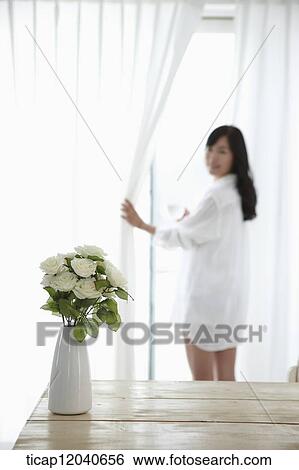 Stock Photograph - woman wearing white shirt and opening the white curtains. Fotosearch