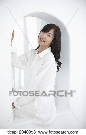 Stock Photo - woman wearing white shirt and sitting on the window . Fotosearch