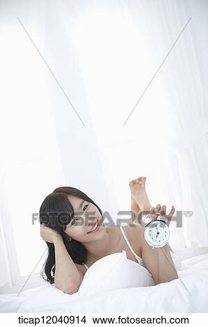 woman wearing white sleepwear and holding a clock on the bed View Large Photo Image Picture - woman wearing white sleepwear and holding a clock on the bed. Fotosearch