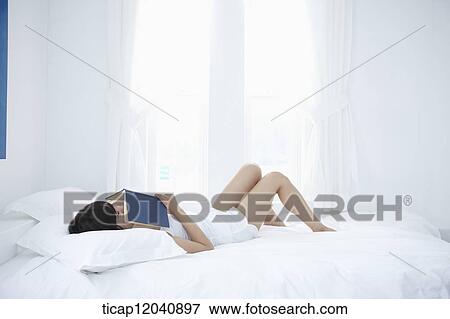 Stock Photo - woman wearing white sleepwear and reading a book on the bed . Fotosearch