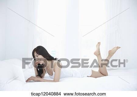 woman wearing white sleepwear and using the laptop on the bed View Large Photo Image Picture - woman wearing white sleepwear and using the laptop on the bed . Fotosearch