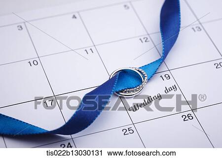 Clip Art - wedding ring on a blue ribbon laying on a calendar. Fotosearch
