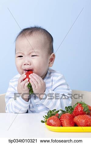 Stock Image - a baby crying while having a strawberry. Fotosearch
