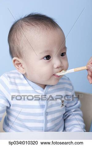 Stock Image - a baby getting food with a spoon. Fotosearch