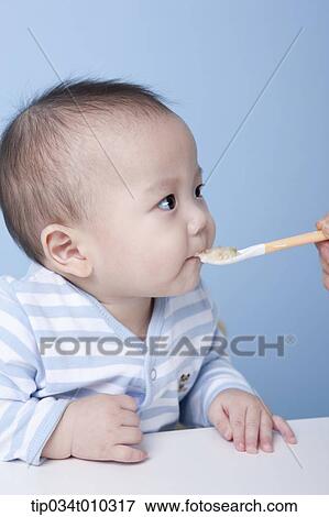 Stock Photo - a baby getting food with a spoon. Fotosearch
