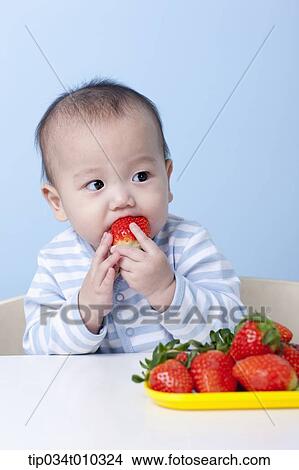 Picture - a baby having a strawberry. Fotosearch