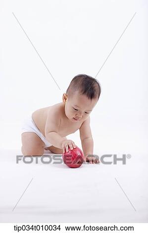 Picture - a baby in diaper crawling to an apple. Fotosearch