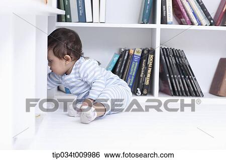 Stock Photograph - a baby playing while sitting under a desk. Fotosearch