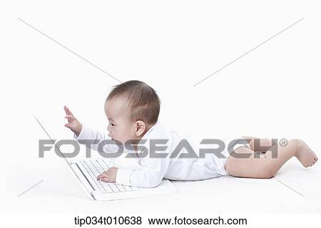 Stock Photo - a baby playing with a laptop while lying on the floor. Fotosearch