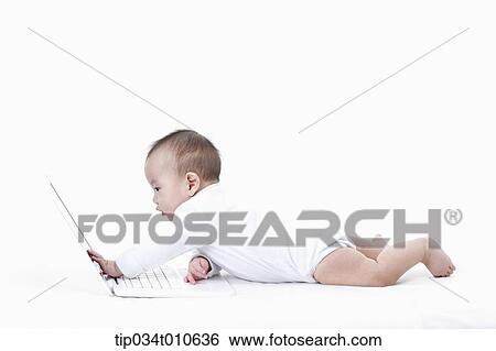 Stock Photograph - a baby playing with a laptop while lying on the floor. Fotosearch