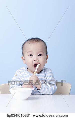 Stock Image - a baby with a bowl and a spoon on table. Fotosearch