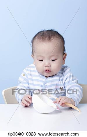 a baby with a bowl and a spoon on table View Large Photo Image Stock Photo - a baby with a bowl and a spoon on table. Fotosearch