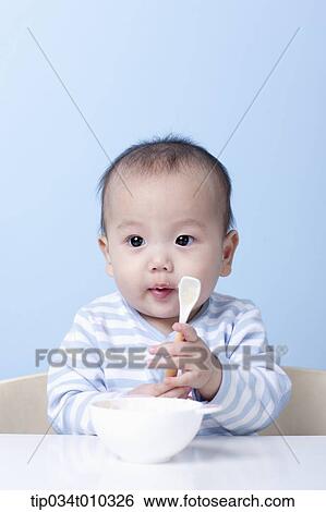 Stock Photograph - a baby with a bowl and a spoon on table. Fotosearch
