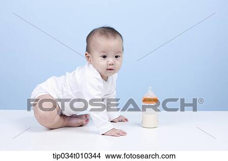 Picture - a baby with a milk bottle in front. Fotosearch