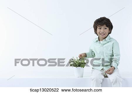 Stock Image - a boy sitting next to a plant. Fotosearch