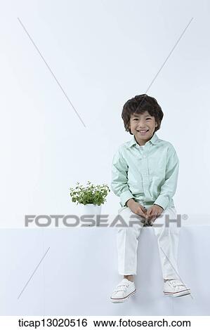 Stock Photograph - a boy sitting next to a plant. Fotosearch