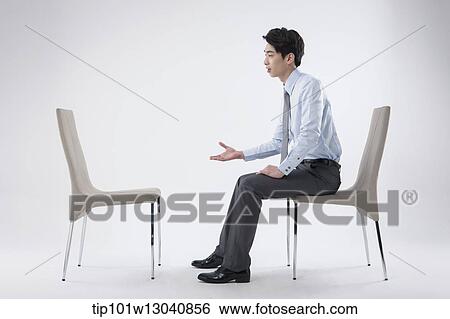 Stock Photograph - a business man sitting and talking to an empty chair. Fotosearch