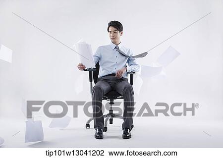 Stock Image - a business man sitting in a chair while papers are flying. Fotosearch
