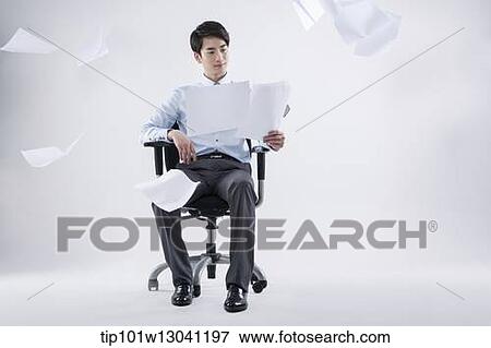 Stock Photo - a business man sitting in a chair while papers are flying. Fotosearch
